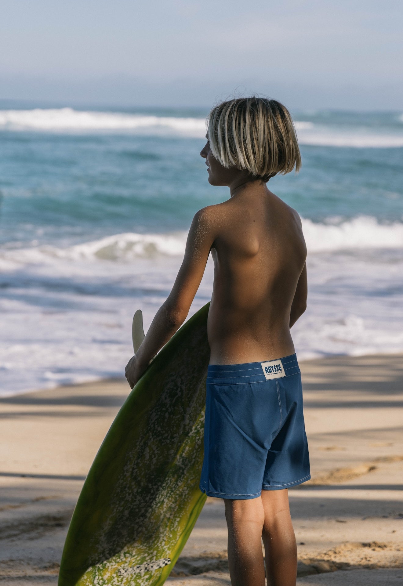 Person holding a surfboard on a beach with ocean waves in the background