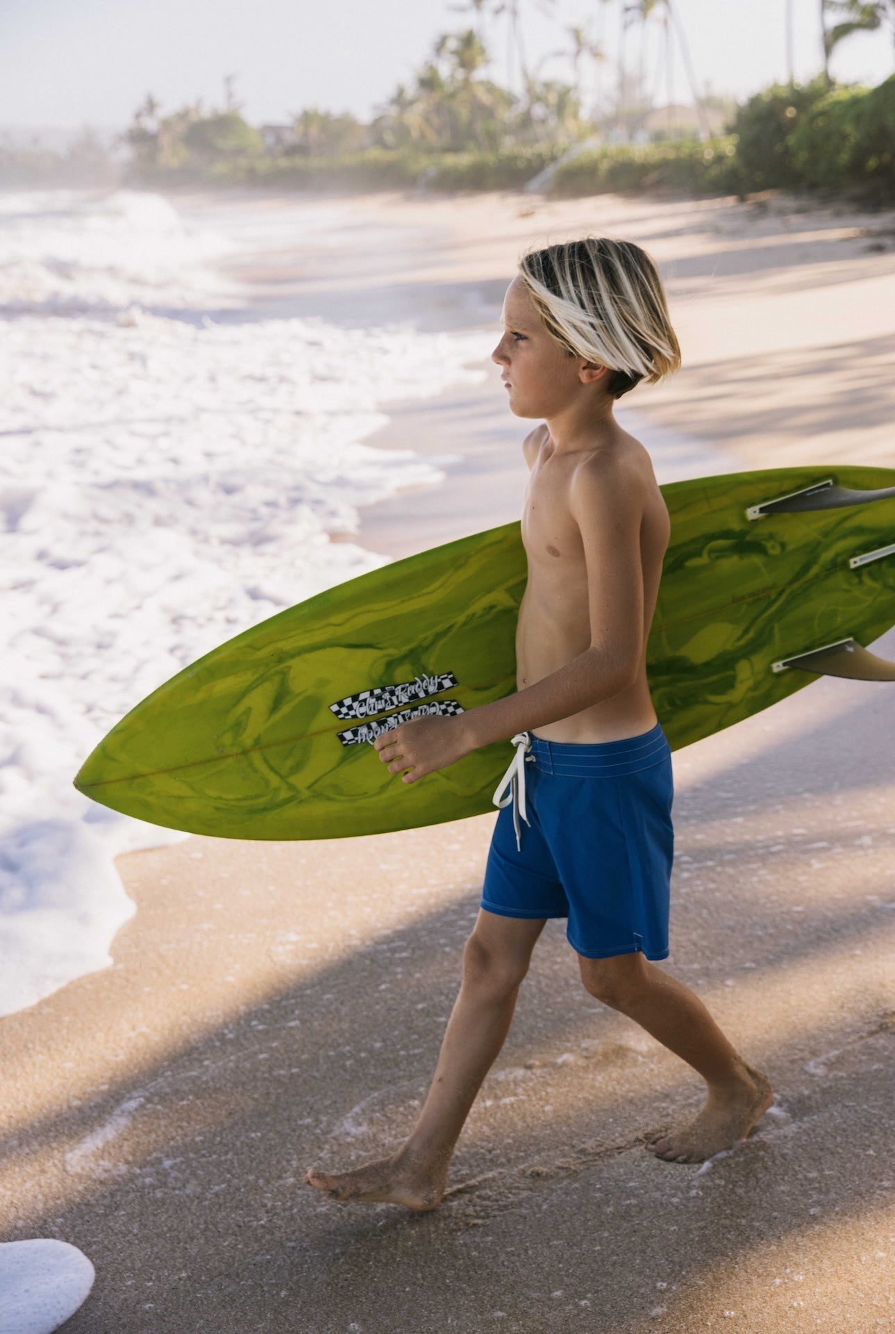 Young boy walking on a beach with a green surfboard
