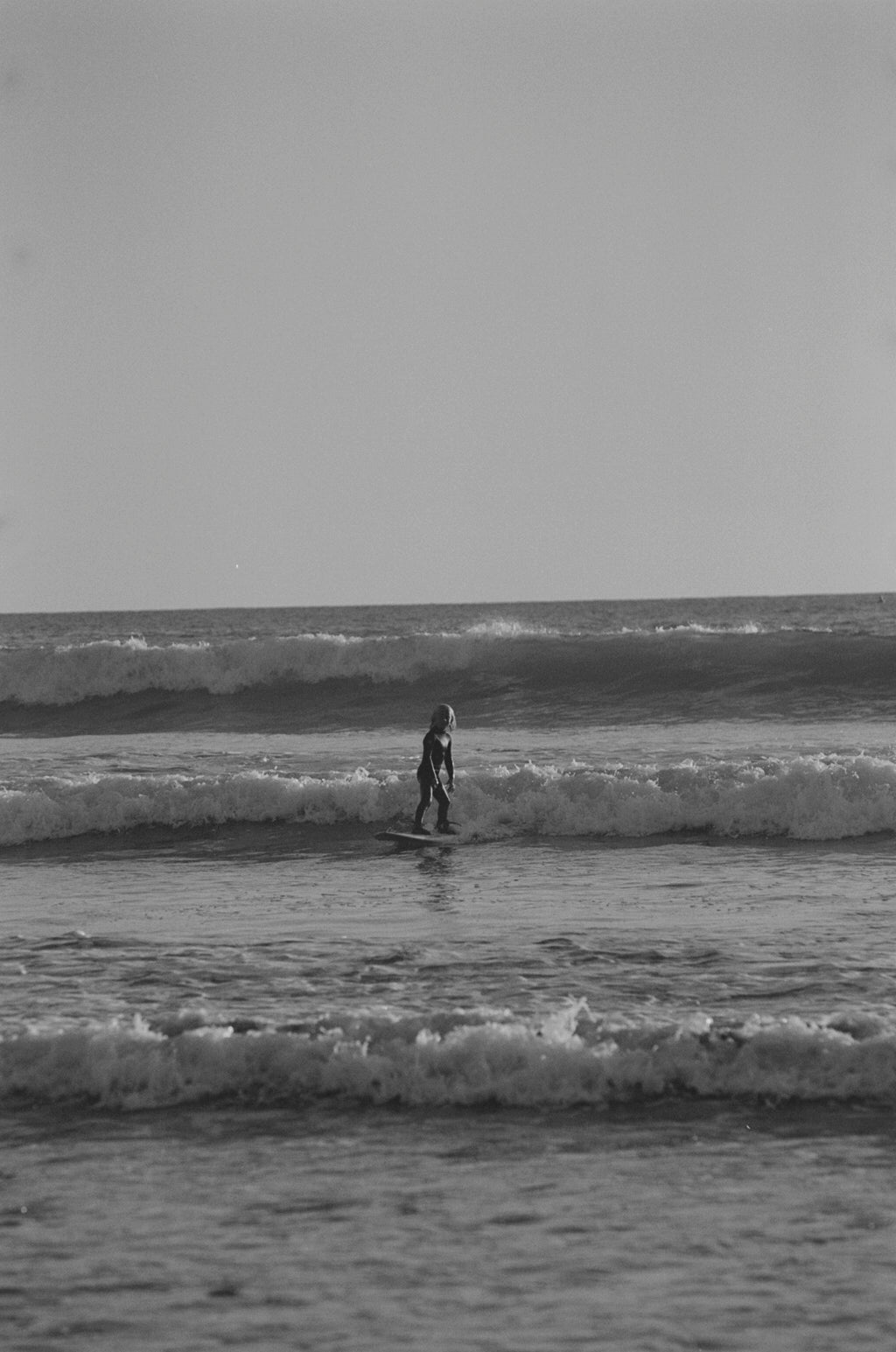 Child surfing on a wave in black and white