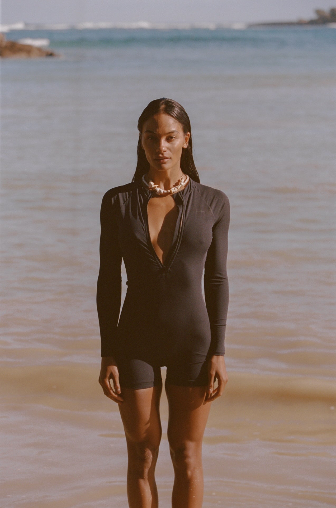 Woman in a black swimsuit standing on a beach with ocean in the background