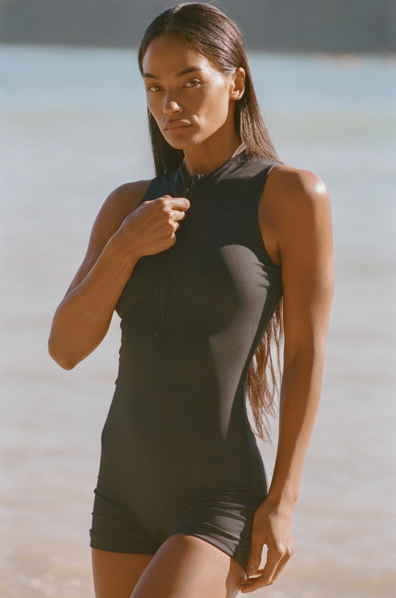 Woman wearing a black sleeveless top and shorts on a beach.
