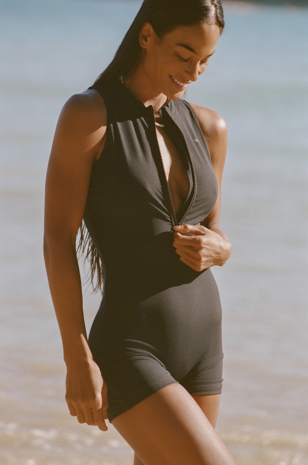 Woman wearing a gray swimsuit standing by a body of water.