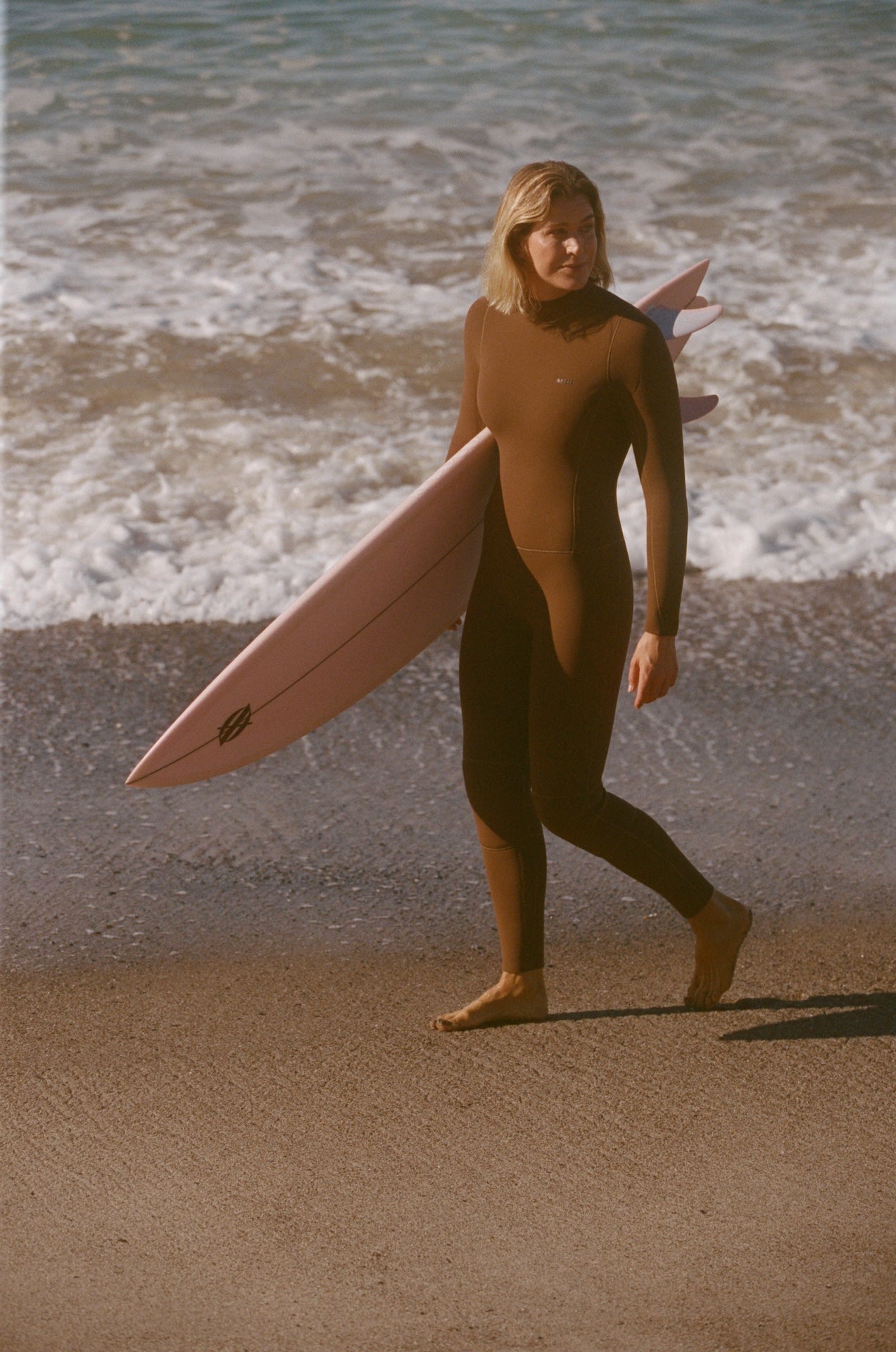 Person in a wetsuit holding a surfboard on a beach