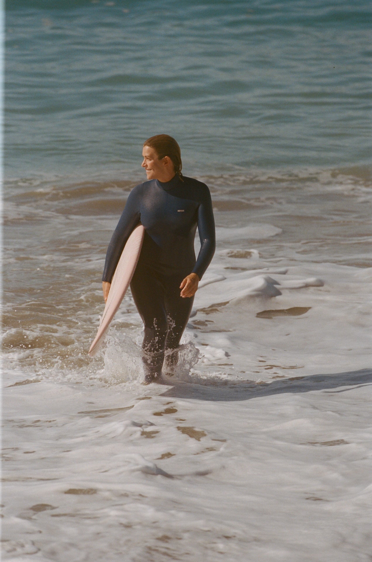 Person in a wetsuit holding a surfboard walking along a beach.