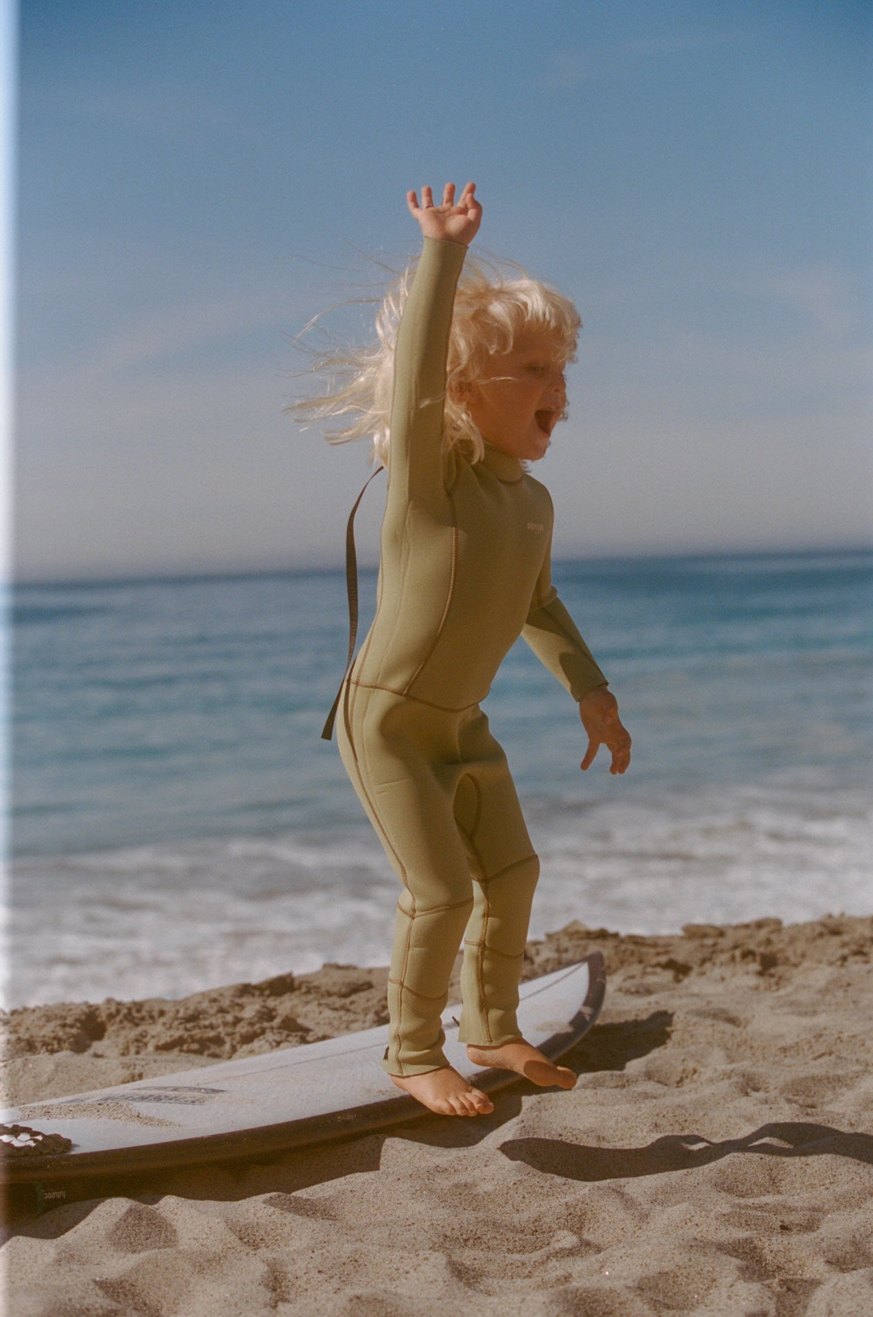Child in a wetsuit standing on a beach with ocean and sky in the background
