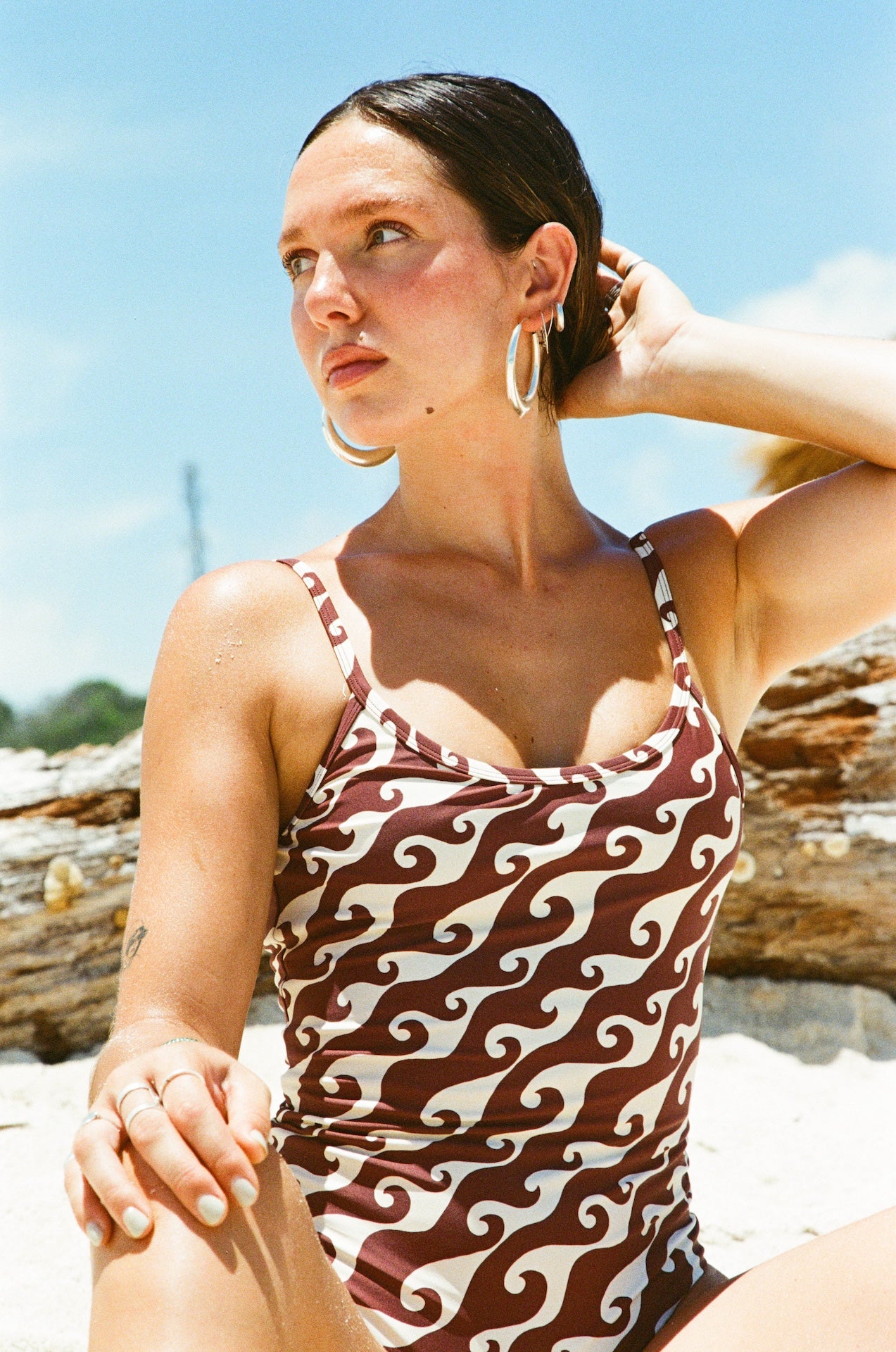 Woman in a patterned swimsuit sitting on a beach with a clear sky.