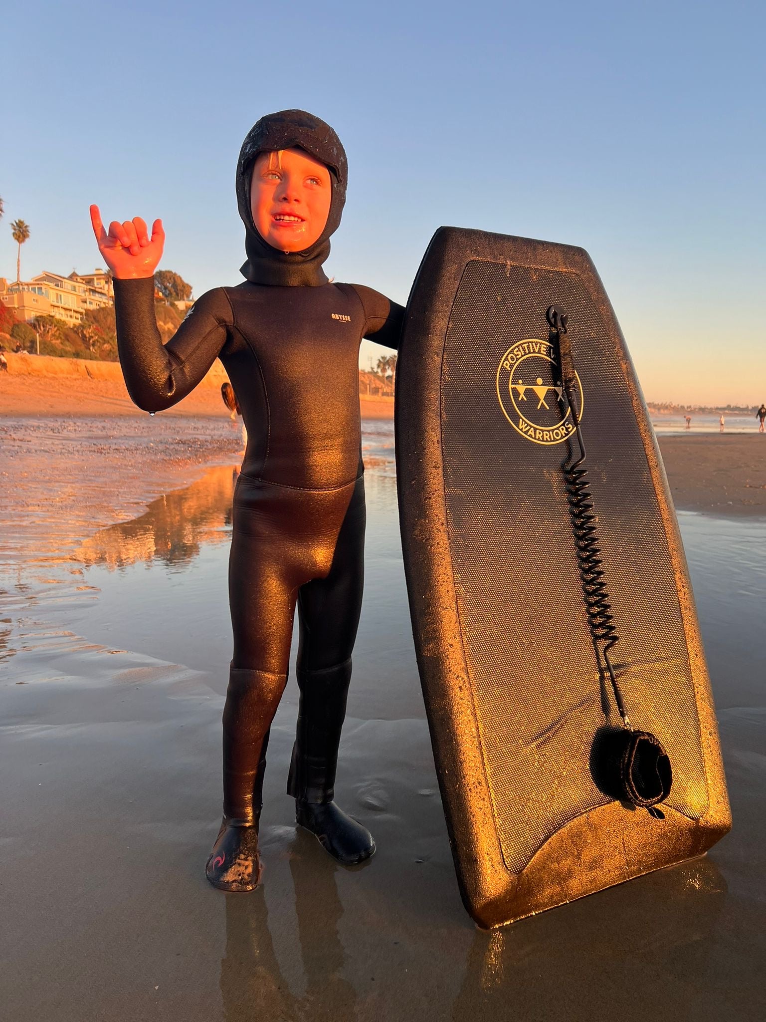 Child in a wetsuit holding a bodyboarding fin on a beach