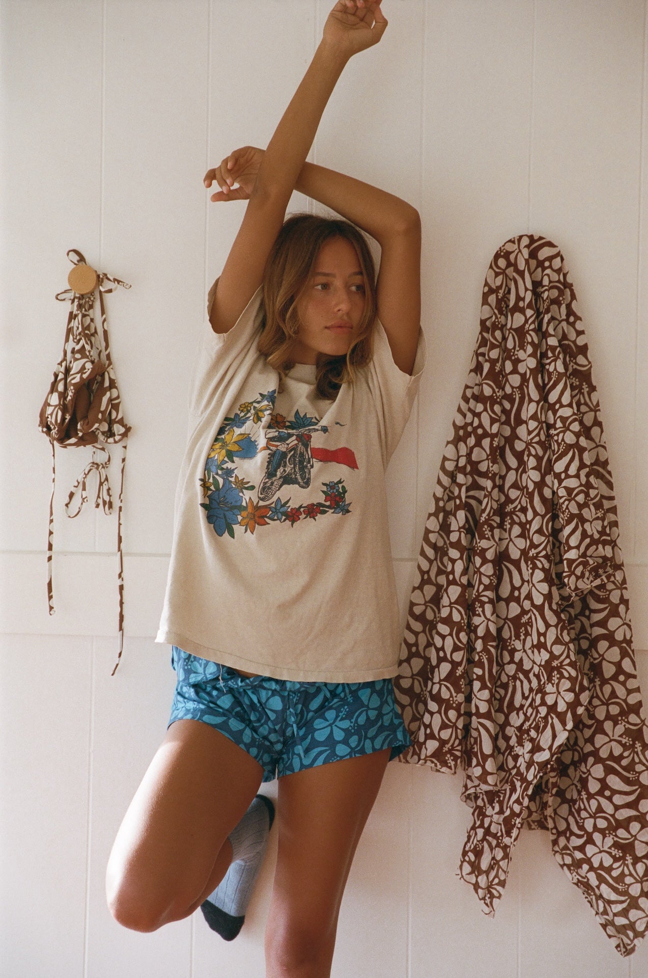 Person wearing a graphic t-shirt and blue shorts with a patterned scarf draped over a chair.
