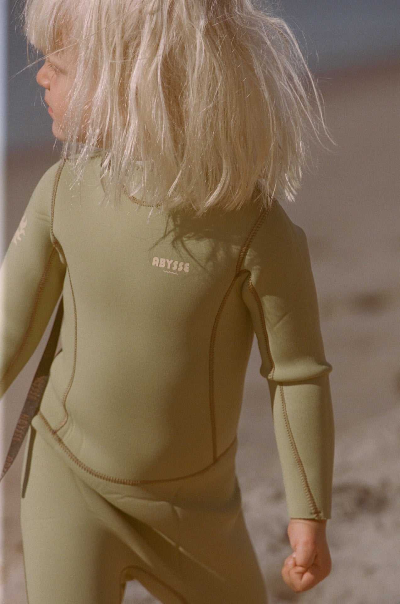 Child wearing a green wetsuit on a beach